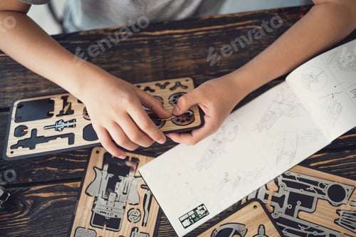 Preview: Curious Kid Sitting At The Table And Using The Instructions While Working With The Wooden