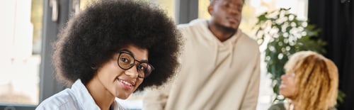 Preview: young woman with glasses smiling at camera with her friends on backdrop, working process banner