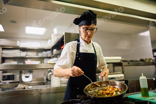 Preview: Female chef preparing food in frying pan in the kitchen.