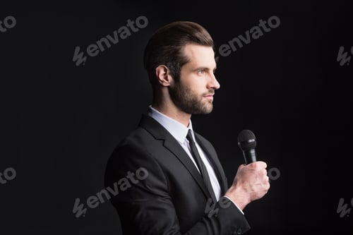 Preview: Young handsome man holding microphone and looking at distance isolated on black