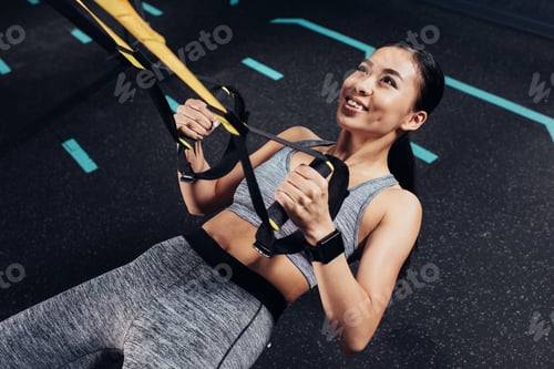 Vista previa: vista de cerca de una chica asiática atlética entrenando con bandas de resistencia y sonriendo en el gimnasio