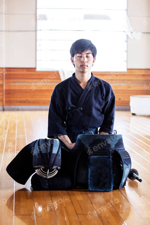 Preview: Male Japanese Kendo fighter kneeling on wooden floor, meditating.