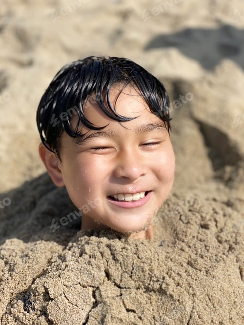 Preview: Child Buried in Sand at Beach Smiles Brightly