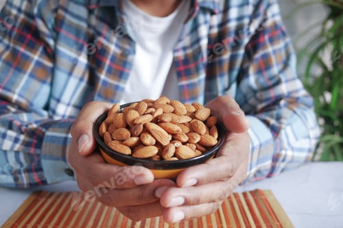 Preview: young man hand hold a bowl of almond nut white sited