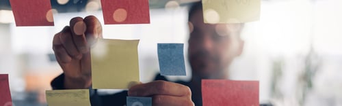 Preview: Close up of businessman is glues sticky notes on motivation board in modern office
