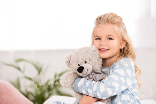 Preview: adorable child hugging teddy bear in bedroom