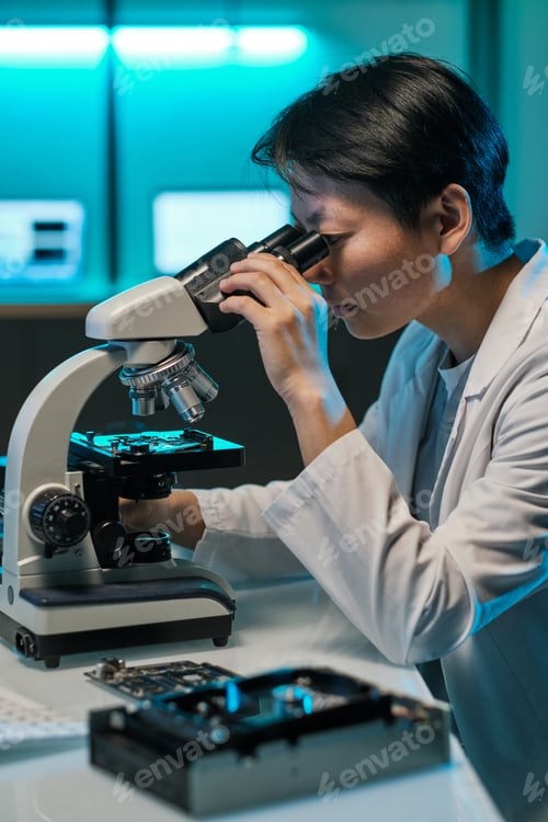 Preview: Young Chinese woman in whitecoat looking in microscope lens