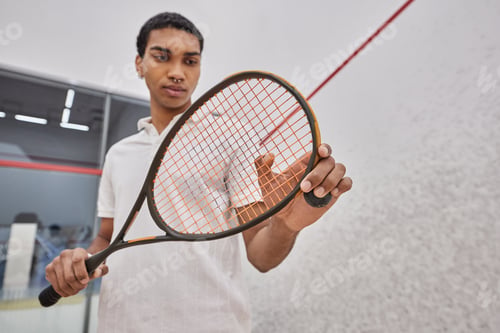 Preview: athletic african american man holding squash ball and racquet while playing game inside of court