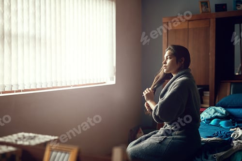 Preview: Shot of a young woman brushing her hair while sitting on her bed in the morning