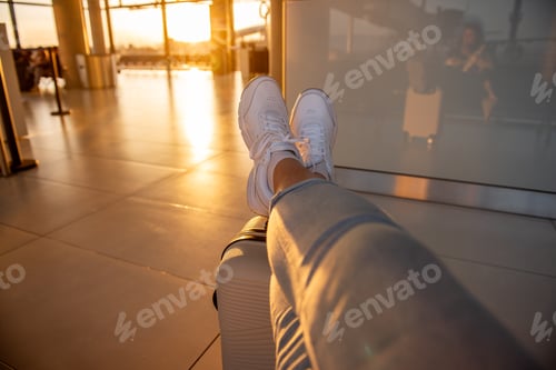 Preview: Tourist relaxing with feet up on luggage at airport during sunset