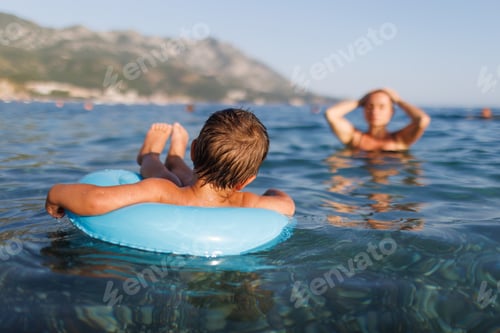 Preview: A little boy swims with an inflatable ring in the sea