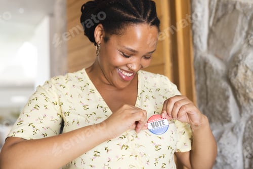 Preview: Young biracial woman pins a 'Vote' sticker on her shirt