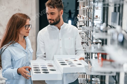 Preview: Bunch of replaceble lenses. Man and woman in the glasses store. Helping to choose product