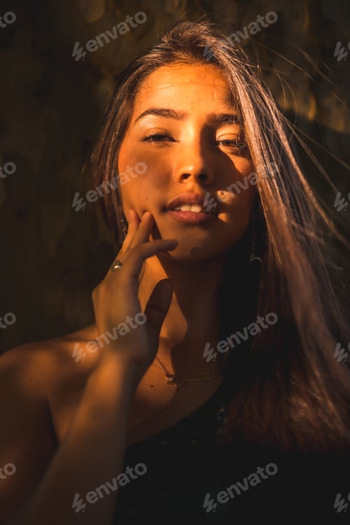 Preview: A young Latina brunette leaning against a tree with a slight light on her face