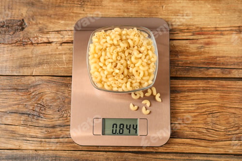 Preview: Modern electronic kitchen scale with bowl of raw pasta on wooden table, top view