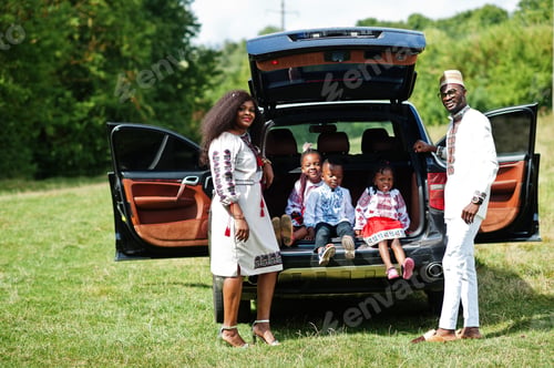 Preview: African family in traditional clothes stand against their car, kids sit on trunk.