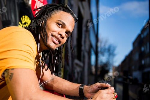Preview: Portrait of young man outdoors, wearing earphones, smiling