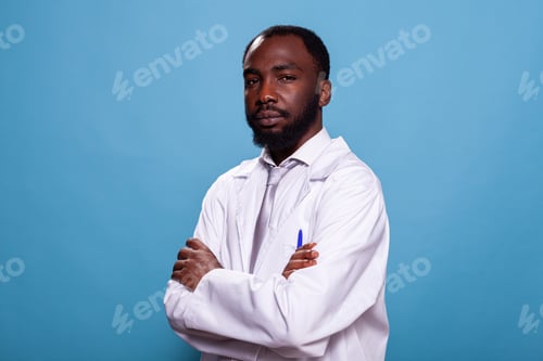 Preview: Portrait of confident medic in laboratory uniform posing with arms crossed on blue background