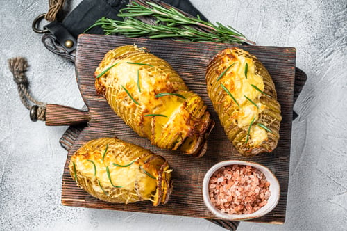 Preview: Roasted hasselback potatoes with cheese, garlic, thyme and rosemary. White background. Top view