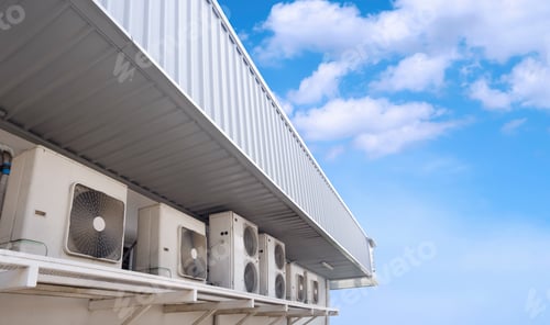 Preview: Row of air conditioner compressors under steel roof eaves of convenience store against blue sky