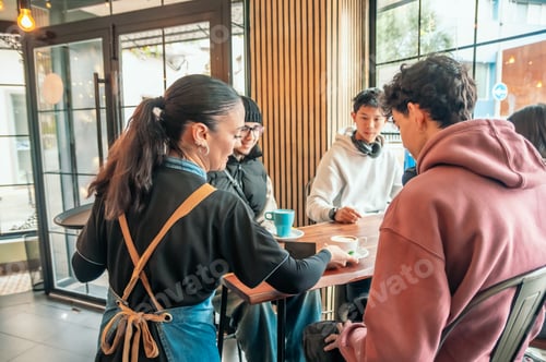 Preview: Friendly waitress pouring coffee for young customers,in sleek contemporary cafe setting