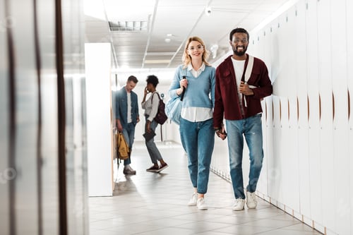 Preview: full length view of smiling multiethnic students holding hands in college