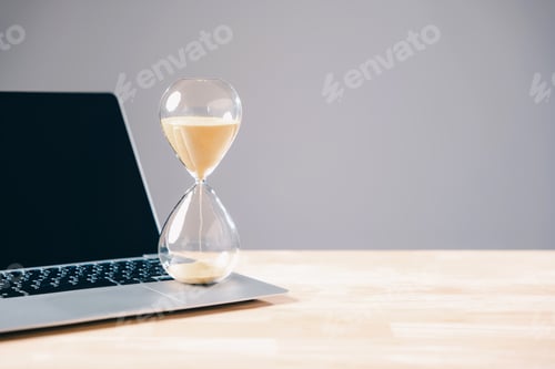 Preview: Hourglass with flowing sand on laptop keyboard symbolizes business deadline, time running out for