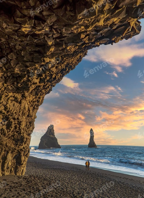Preview: Young couple walking on a sandy Reynisfjara Beach at sunset in Iceland
