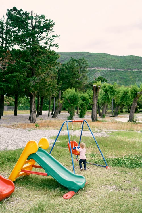 Preview: Little girl holds on to a swing in the park with her hands. Side view