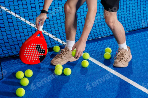 Preview: Padel training session with player collecting balls near net on indoor court