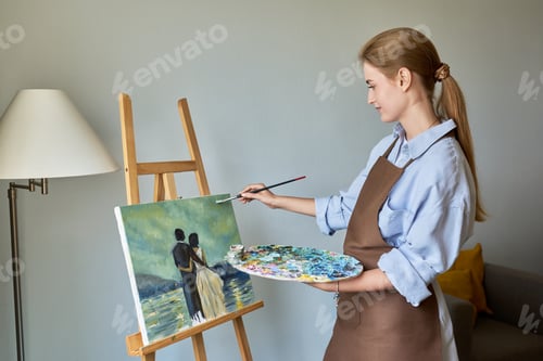Preview: Young pretty female artist painting with acrylics on an easel