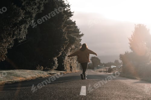 Preview: young caucasian woman walking backwards happy and calm with arms outstretched along a quiet long