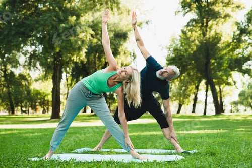 Preview: Flexible fit healthy mature couple training together on fitness mat outdoors. Stretching exercises