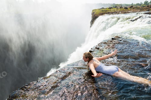 Preview: Young girl in the water at the Devils Pool lying on her front, arms spread out