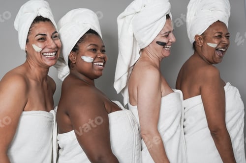 Preview: Multi generational women enjoy spa day together with beauty face mask while wearing towels