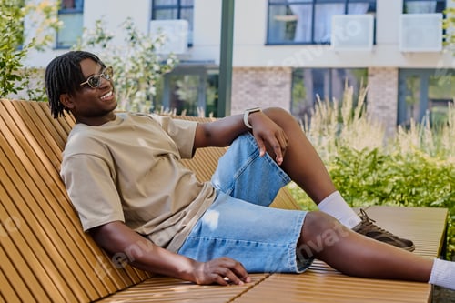 Preview: Handsome young man enjoying a sunny day while sitting comfortably on a stylish bench