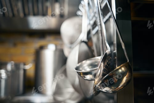 Preview: Focus on hanging skimmers and ladles and blurred table with saucepans