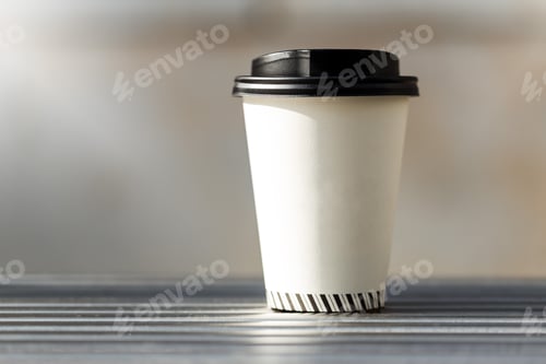 Preview: Disposable coffee cup on bench with blurred city in background.
