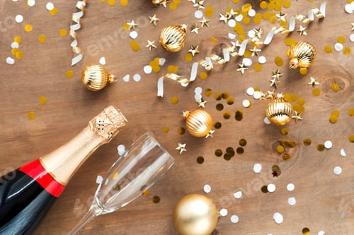 Preview: Champagne bottle and glass with shiny golden confetti on wooden background