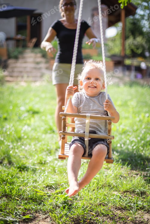 Preview: Happy mother pushing laughing son on swing in backyard