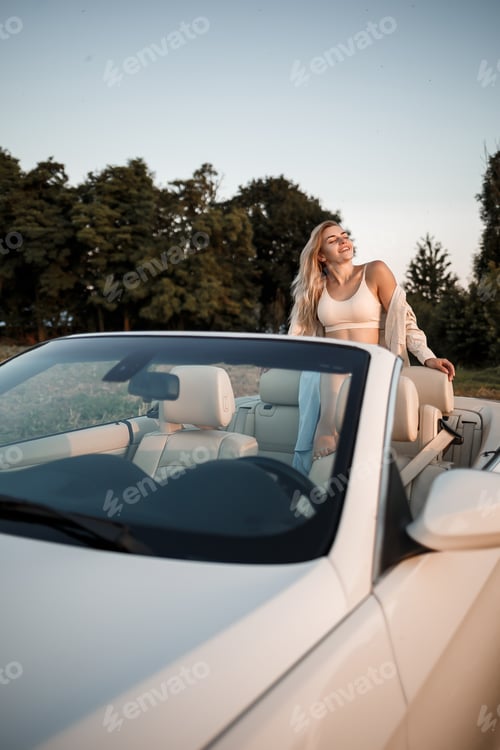 Preview: A glamorous luxury girl with blonde hair smiling while sitting on a white convertible