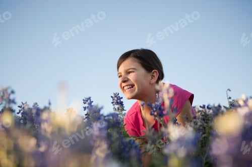 Preview: A girl sitting in a field of tall grass and blue wild flowers.
