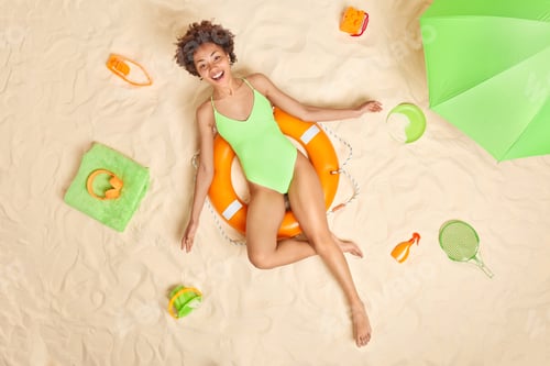 Preview: Joyful slim female tourist spends summer vacation at beach dressed in green swimsuit poses on inflat