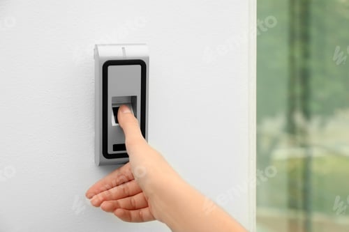 Preview: Young woman scanning fingerprint on alarm system indoors