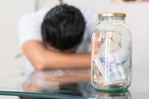 Preview: crestfallen young man with his savings in a glass jar on the table, banknotes inside a glass jar
