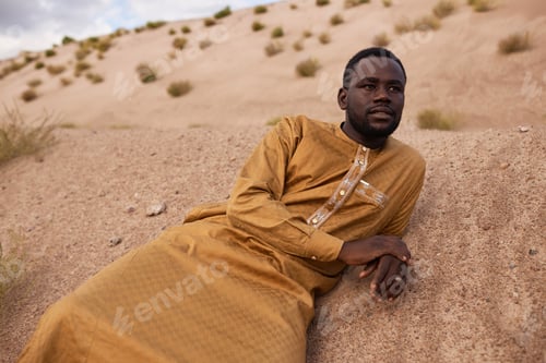 Preview: African American Man in Long Kaftan Dress Lying on Sand Dunes