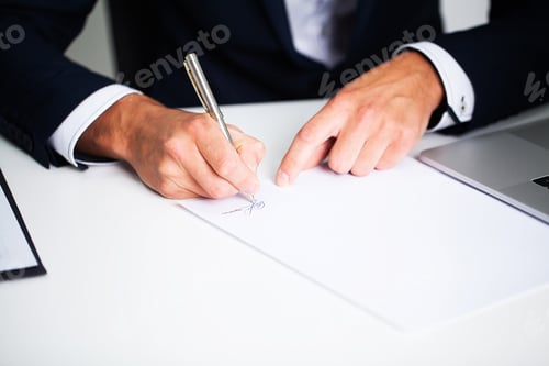 Preview: Businessman sitting at office desk signing contract