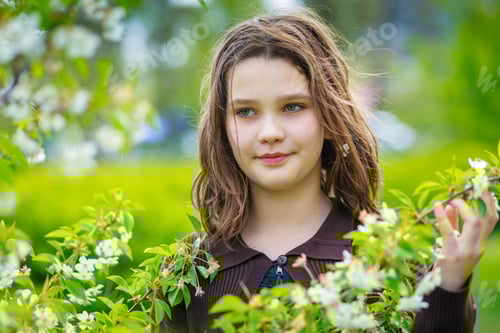 Preview: Beautiful girl among cherry flowers in spring. Portrait of a girl with brown hair and green eyes.