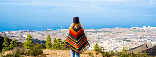 Preview: Woman admiring beautiful panorama landscape and wearing colorful trendy poncho. Tourist
