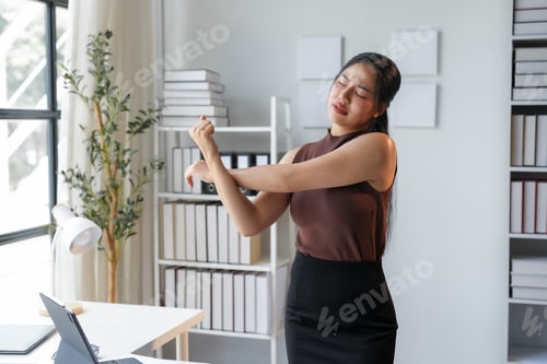 Preview: Young office manager is relieving muscle tension by stretching her arms while standing in her office